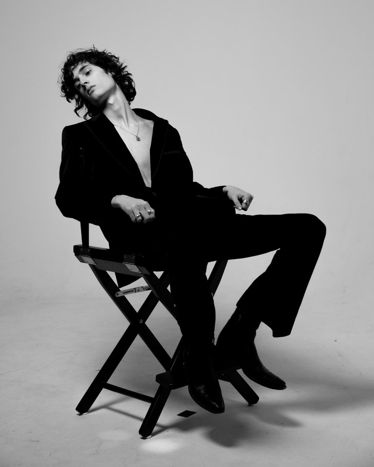 En ung man i svart lutar sig tillbaka i en regissörsstol.