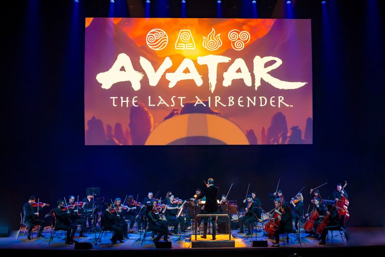 En stråkorkester på en scen under en filmduk med texten: Avatar: The Last Airbender.