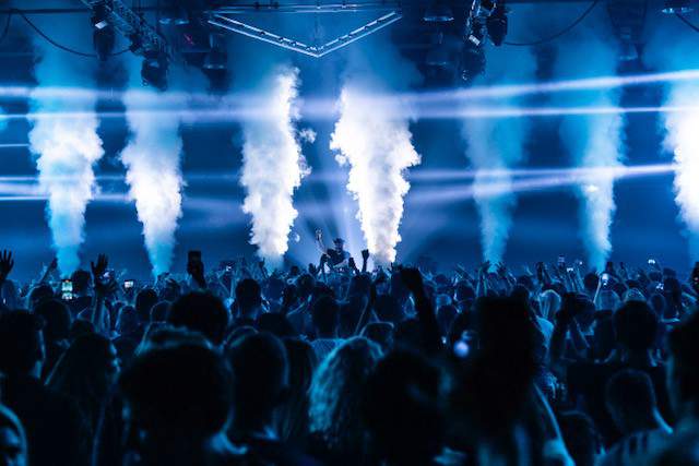 En konsertlokal med mycket publik och rök som kommer upp från scenen.