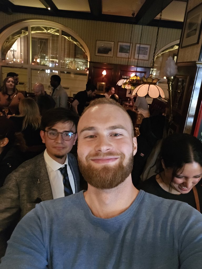 En leende man vid ett socialt mingel på en bar, med andra gäster i bakgrunden