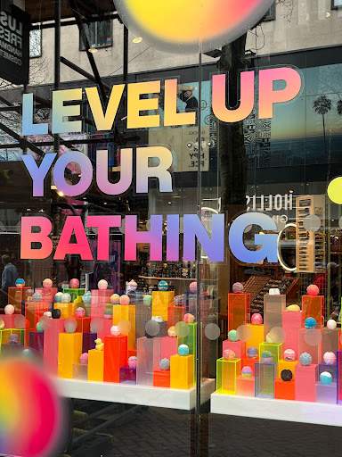 Texten "Level up your bathing" i skyltfönstret med badbomber i olika färger.