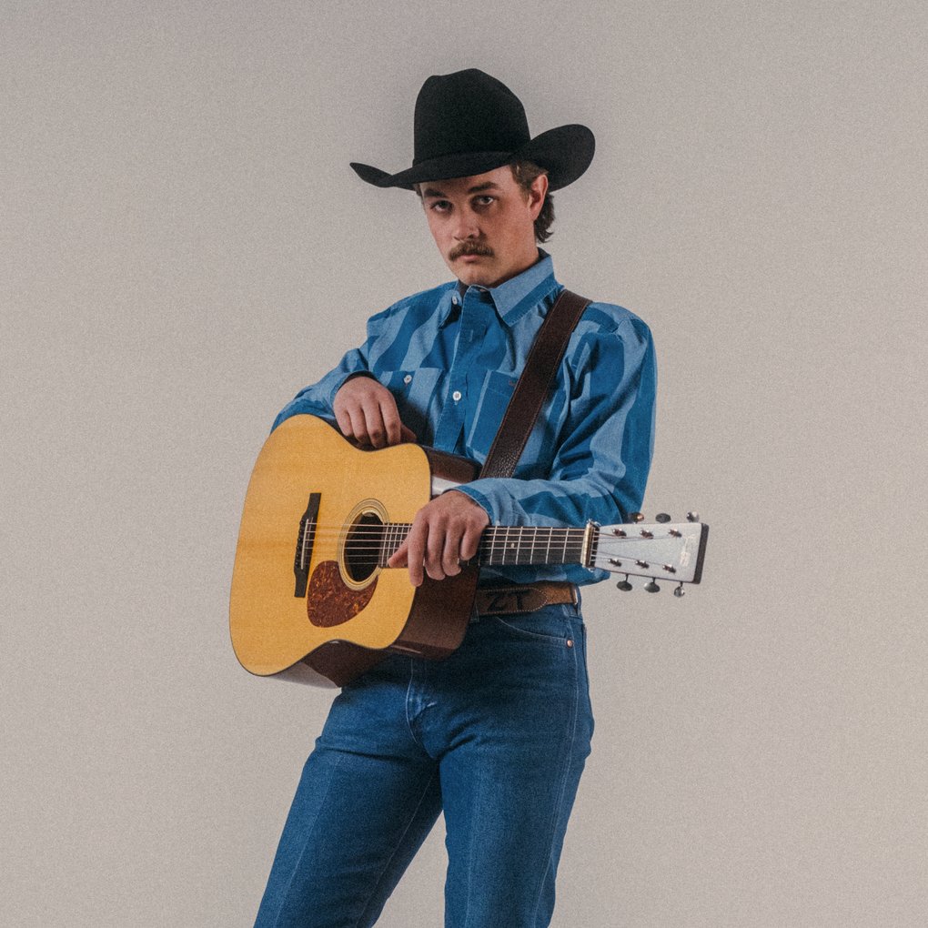 En man i cowboyhatt som håller i en gitarr.